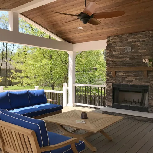 Covered porch with wood-plank ceiling, ceiling fan, stone fireplace, and cushioned seating
